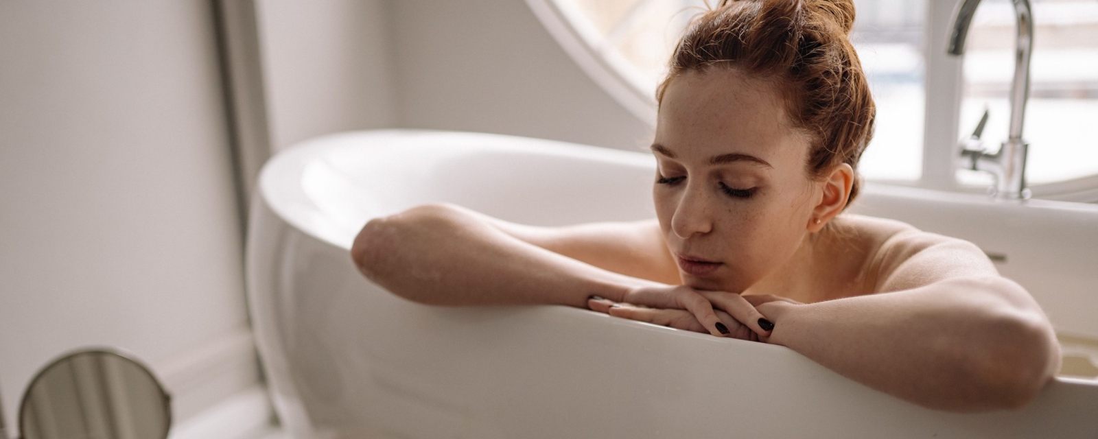 Red head woman relaxing in a white and free standing bathtub by Studium Dekor.